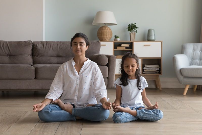 Silent_Indian_woman_and_preschooler_5s_serene_daughter_meditating_seated_in_lotus_position_on_warm_floor_in_modern_living_room._Good_life_habit,_healthy_lifestyle,_yoga_practice_with_children_at_home
