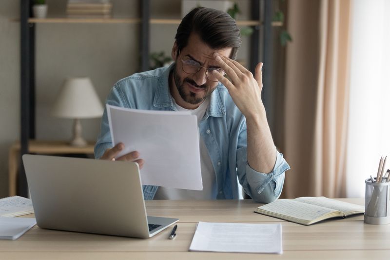 Confused_shocked_self_employed_businessman_holding_paper_letter_informing_about_accumulated_bank_debt_unexpected_financial_problem._Upset_stressed_young_male_enterpreneur_get_loan_application_rejected