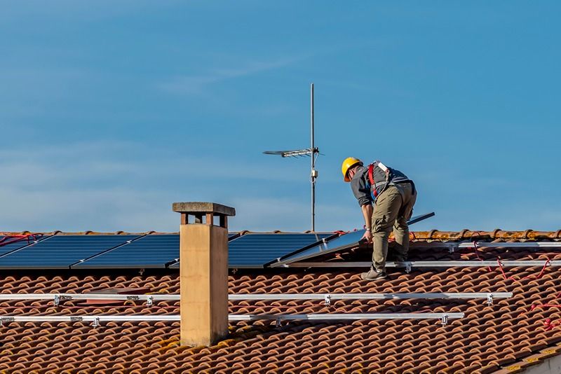 A_technician_lays_the_solar_panels_of_a_photovoltaic_system_on_top_of_a_red-tiled_roof