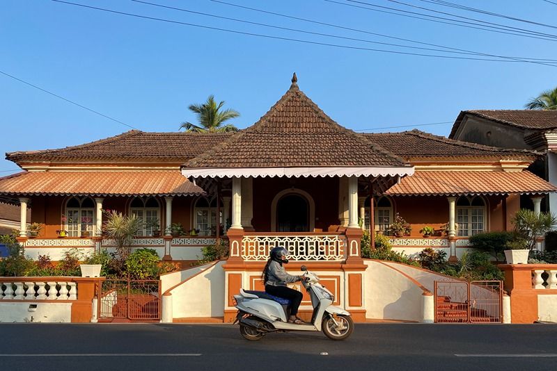 Margao,_India_-_January_21_2023:_A_man_rides_a_two_wheeler_scooter_past_an_old_traditional_house_in_Goa.