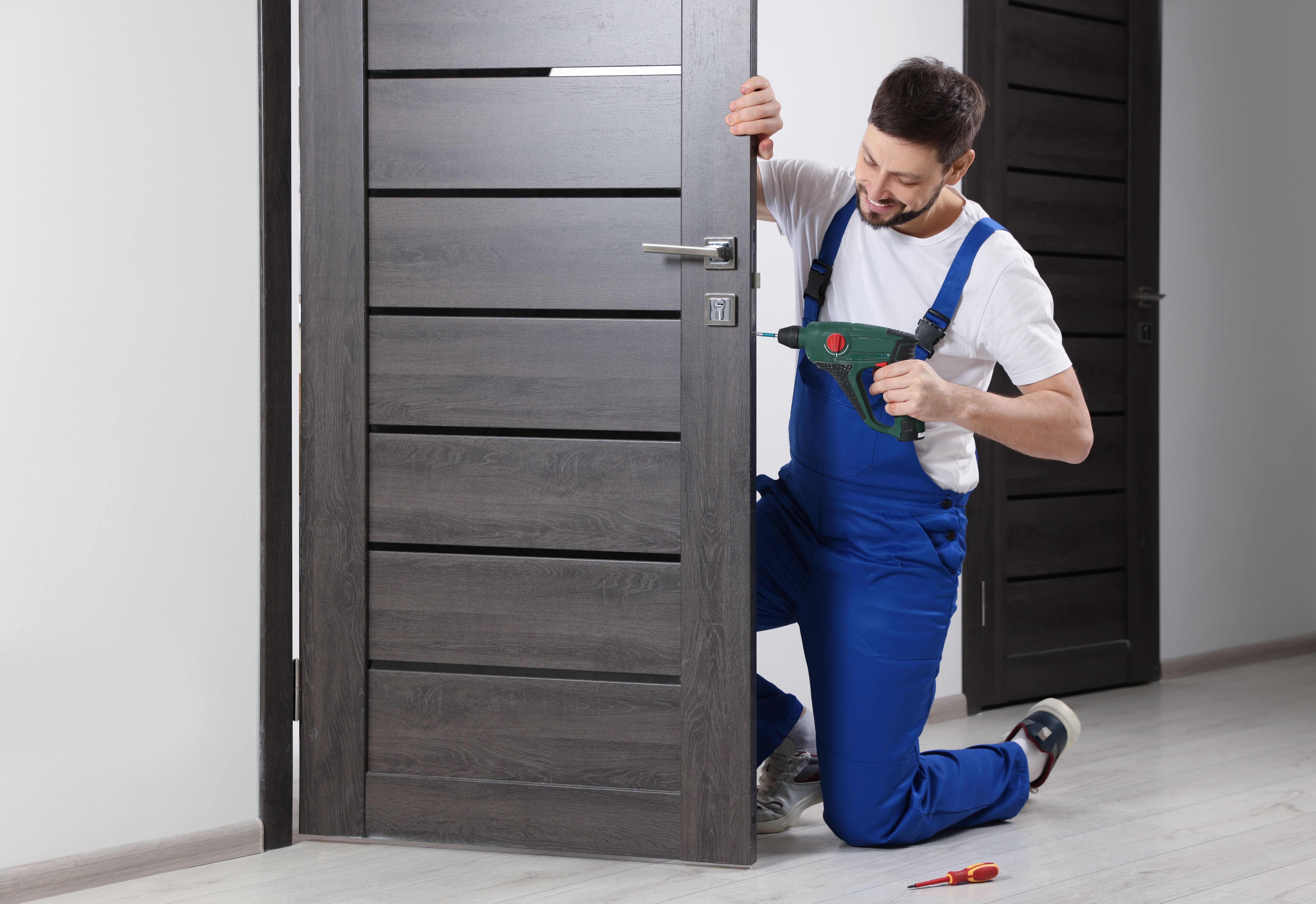 Worker_in_uniform_with_screw_gun_repairing_door_lock_indoors