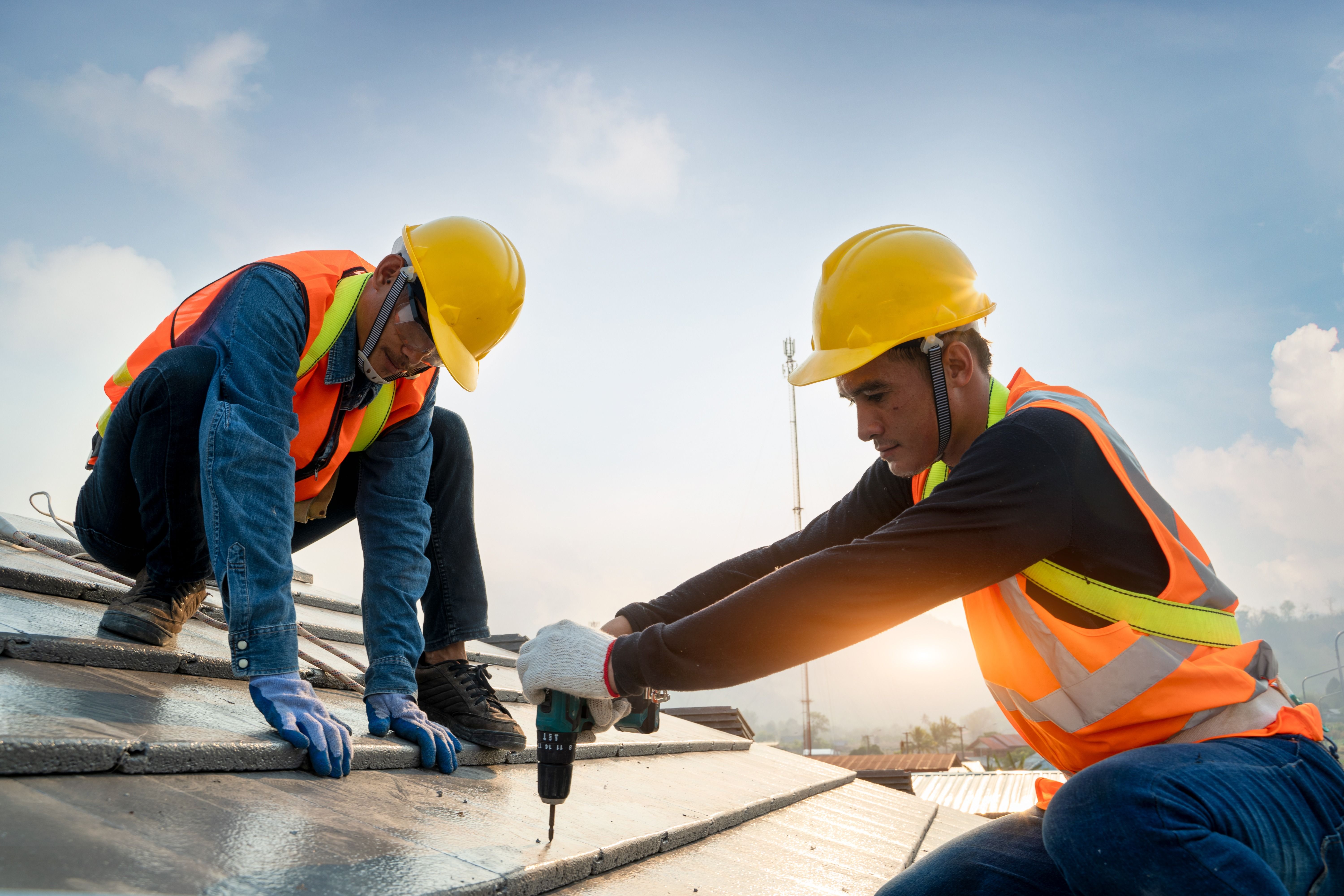 Construction_worker_wearing_safety_harness_belt_during_working_on_roof_structure_of_building_on_construction_site,Roofer_using_air_or_pneumatic_nail_gun_and_installing_concrete_roof_tile_on_top_roof.