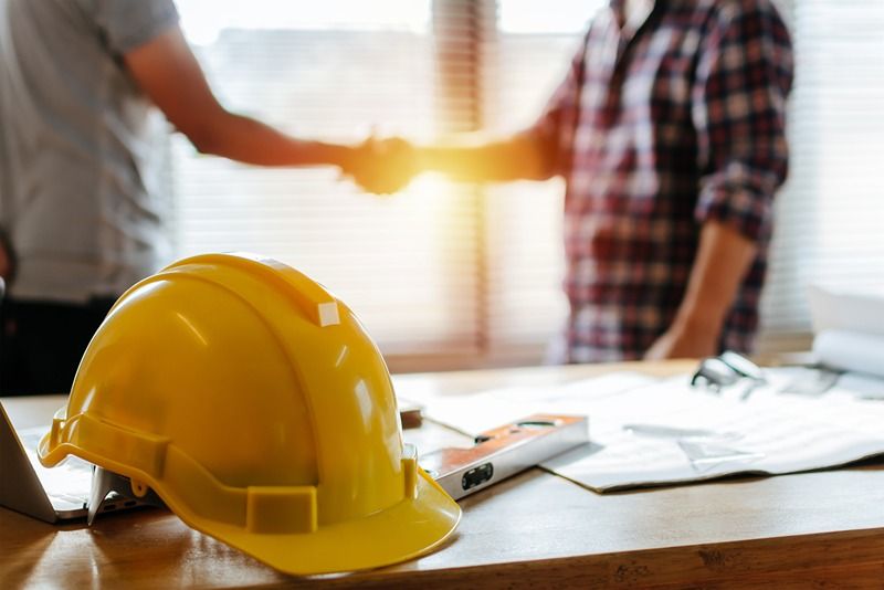 yellow_safety_helmet_on_workplace_desk_with_construction_worker_team_hands_shaking_greeting_start_up_plan_new_project_contract_in_office_center_at_construction_site,_partnership_and_contractor_concept