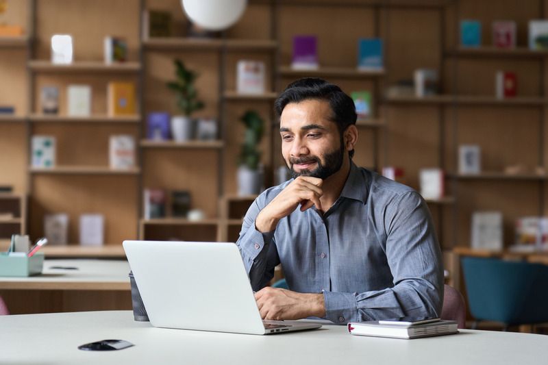 Young_adult_happy_smiling_Hispanic_indian_student_wearing_headphones_talking_on_online_chat_meeting_using_laptop_in_university_campus_or_at_virtual_office._