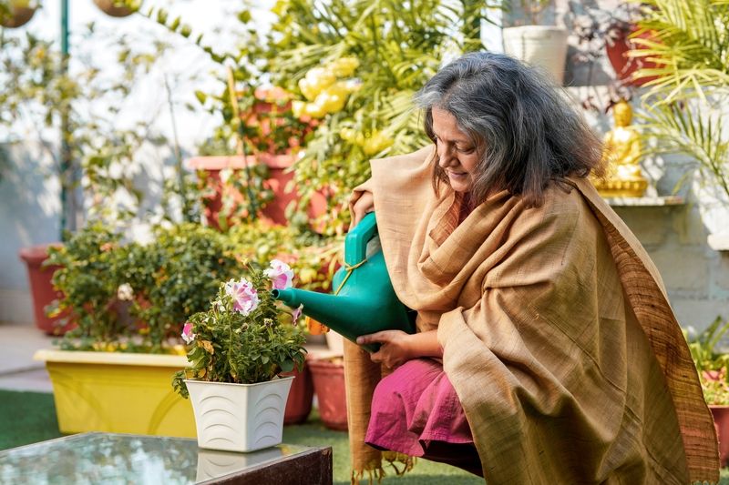 Indian_Senior_woman_watering_the_flowers_in_the_garden.