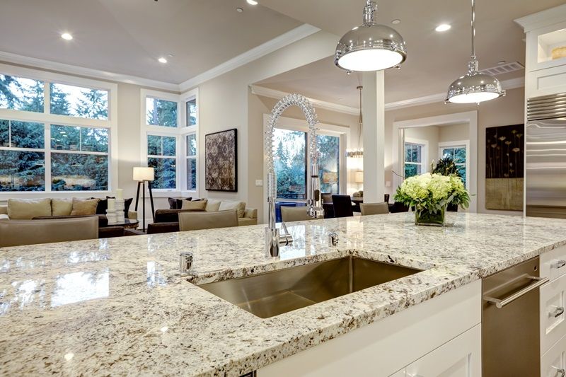 White_kitchen_design_features_large_bar_style_kitchen_island_with_granite_countertop_illuminated_by_modern_pendant_lights