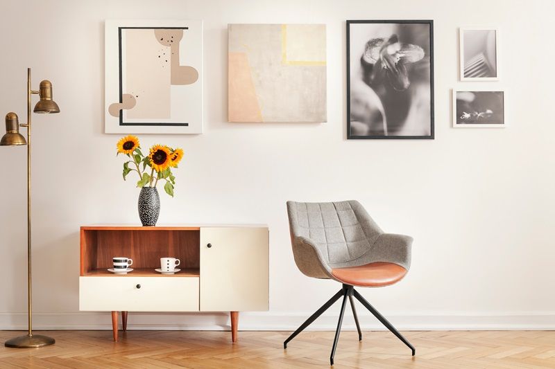 Grey_armchair_next_to_cupboard_with_sunflowers_in_white_room_interior_with_gallery